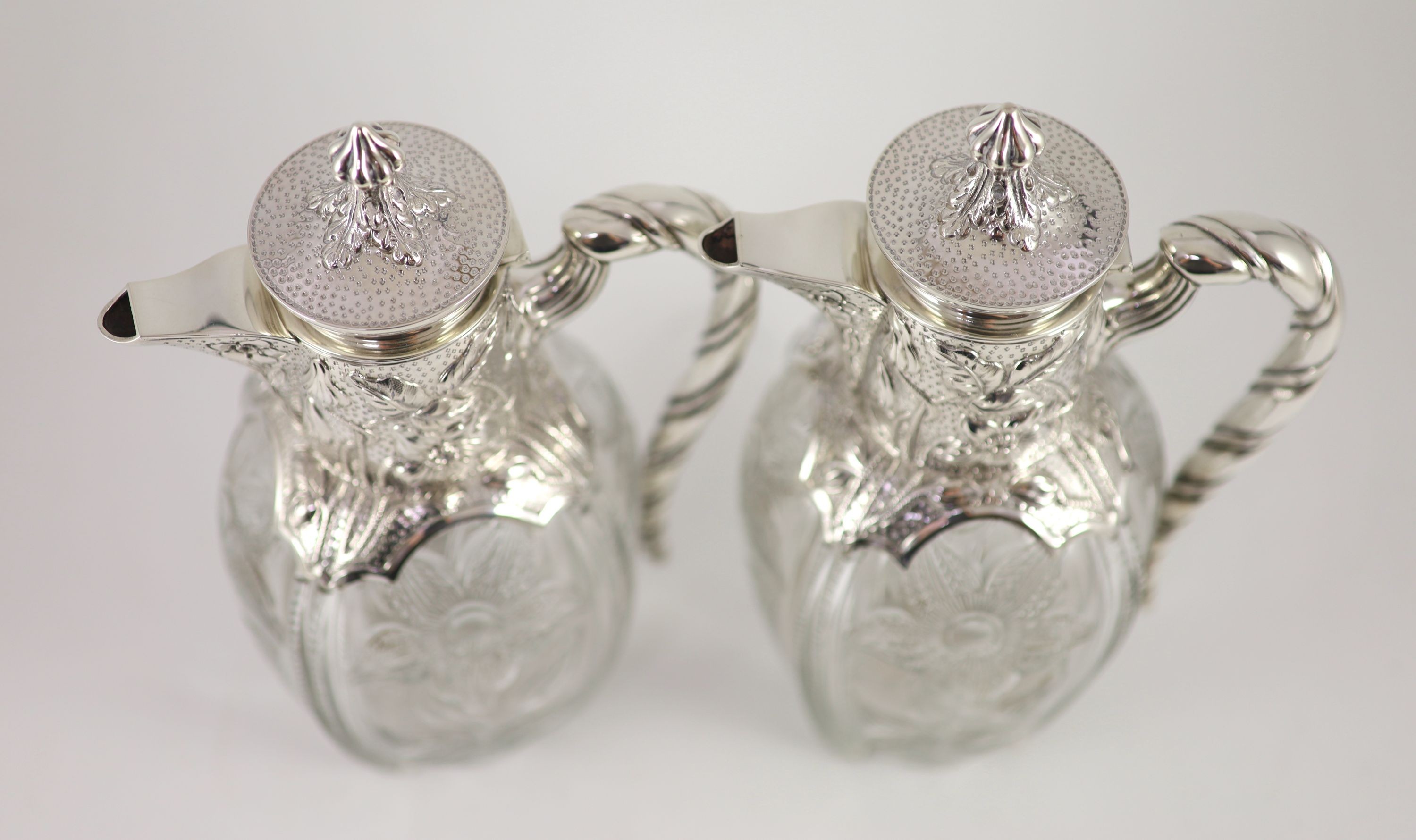 A good pair of late Victorian silver mounted ‘rock crystal’ glass claret jugs, with hinged covers, by John Grinsell & Sons